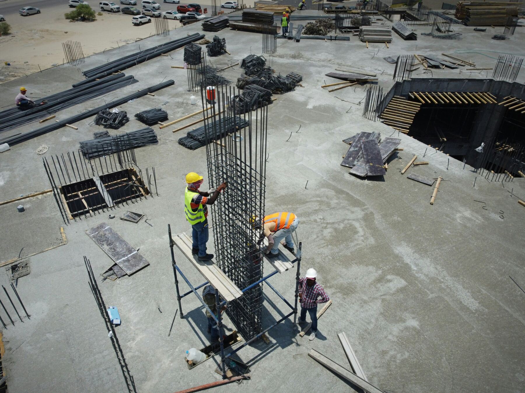 Site workers fixing a reinforcement cage for a concrete column on a building slab, seen from above