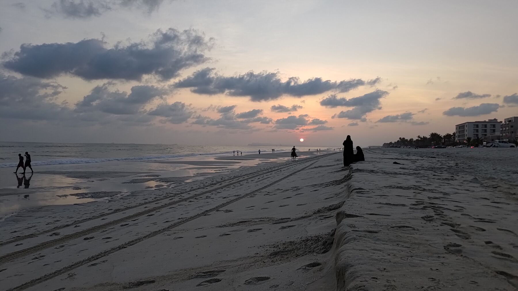 Salalah beach at sunset, with calm wet sand and a low sun under broken cloud