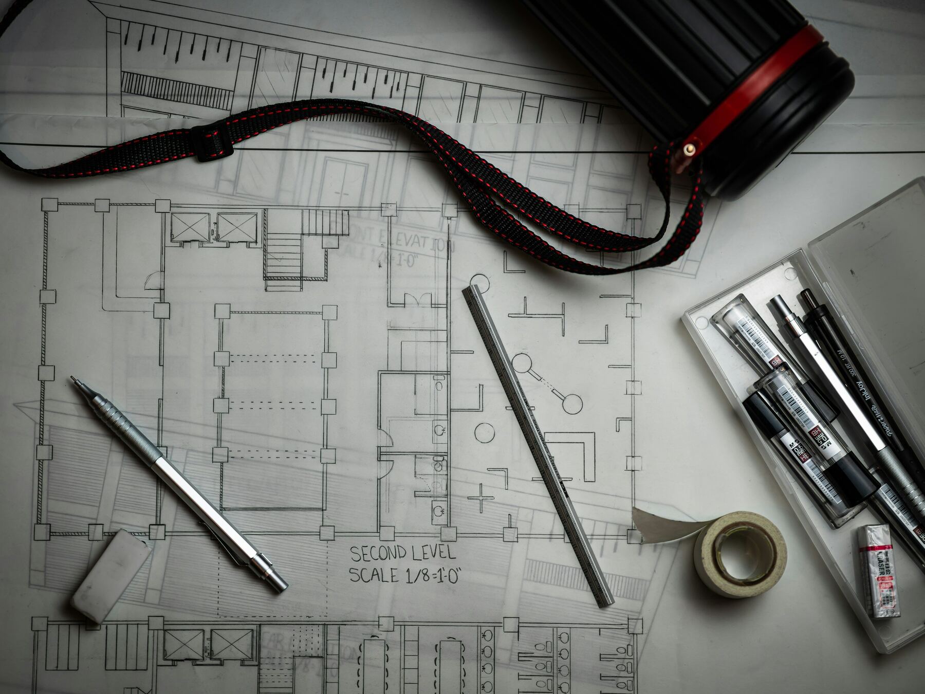 An architectural floor plan on a desk with drafting pencils, pens and tape