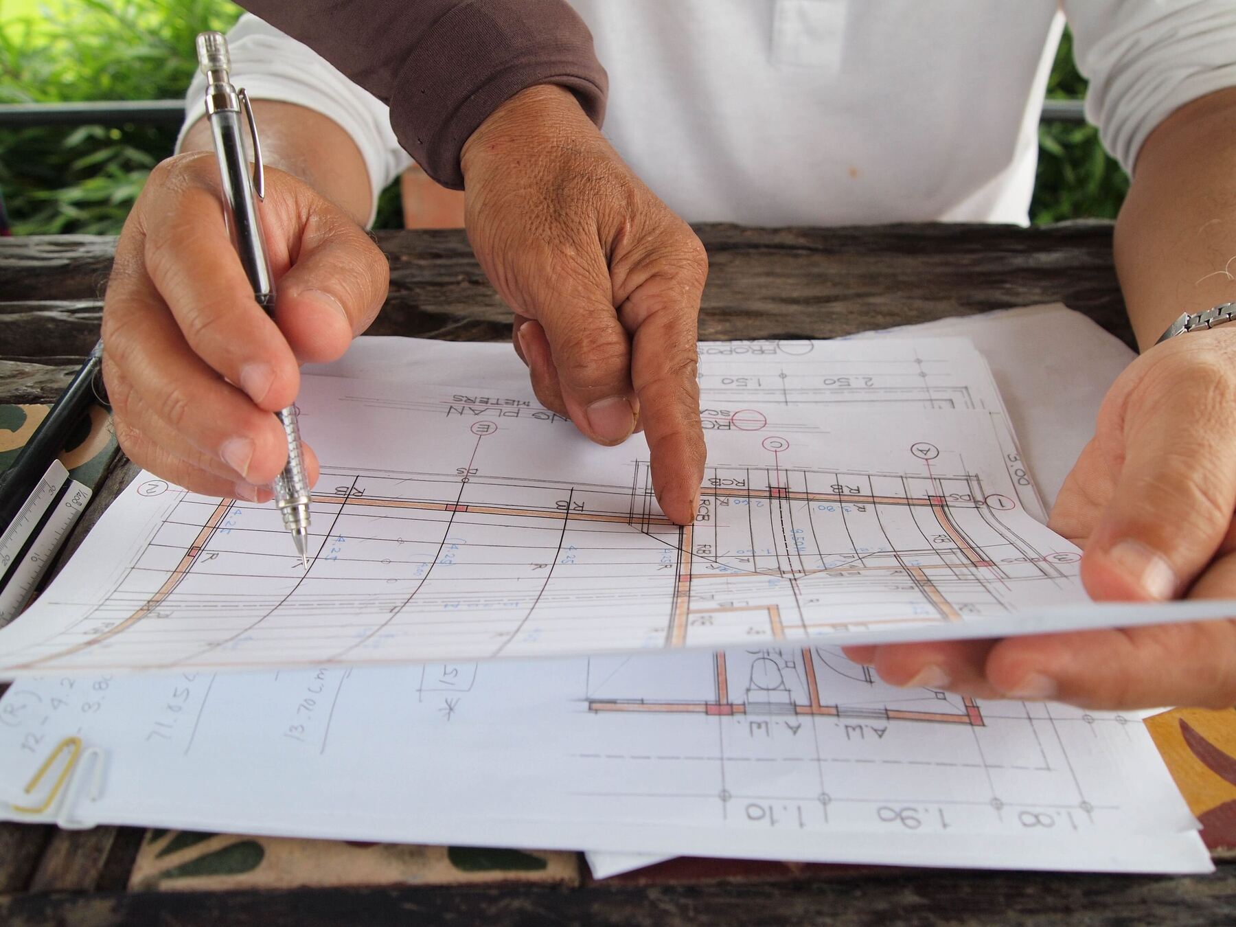 Hands marking up construction drawings with a pen on a table